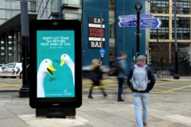 People walking in the street next to an advertising board.
