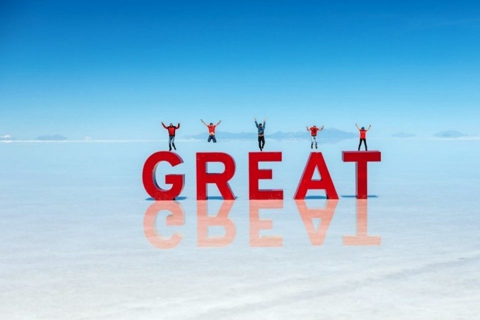 Red letter blocks in the middle of a lake with five people jumping above the letters GREAT.