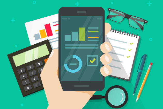 a hand holding a phone with infographics on the screen and a calculator, a notepad, a pen and pencil, glasses and a magnifying glass in the background.