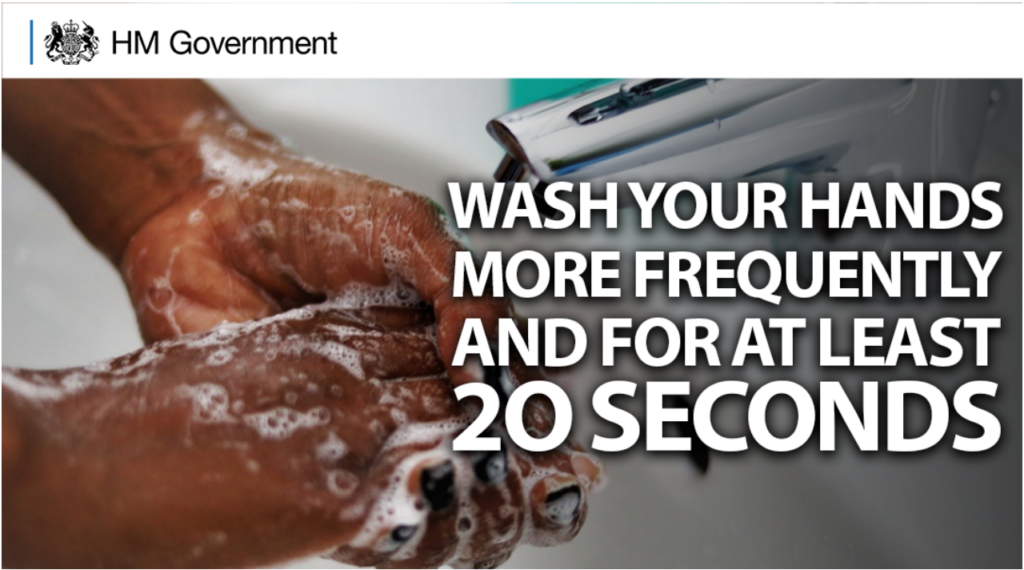 A public health graphic from HM Government encouraging regular handwashing.
Top header: A clean white bar across the top features the official black HM Government coat of arms logo and text on the left side.
Main image: The background shows a close-up photograph of a person actively washing their hands under a silver tap with visible soap suds.
Text overlay: Large, bold white text with a slight drop shadow covers the right side of the image, reading: "WASH YOUR HANDS MORE FREQUENTLY AND FOR AT LEAST 20 SECONDS".