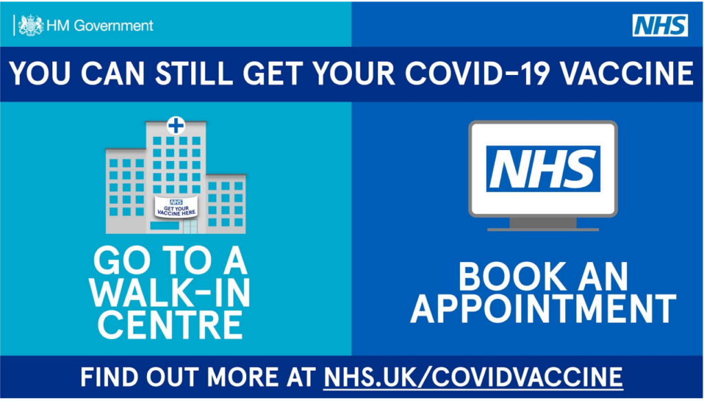 An official HM Government and NHS promotional graphic encouraging people to get vaccinated against COVID-19. The banner image is split vertically into a light blue side on the left and a dark blue side on the right.
Top Header: A solid dark blue band reads "YOU CAN STILL GET YOUR COVID-19 VACCINE" in bold white text. The HM Government logo sits in the top-left corner and the NHS logo sits in the top-right corner.
Left Section (light blue background): Features a simple vector illustration of a grey hospital building with a blue cross on top and a white banner reading "NHS GET YOUR VACCINE HERE". Below the building, large bold white text reads "GO TO A WALK-IN CENTRE".
Right Section (dark blue background): Features a simple vector illustration of a grey computer monitor displaying the blue and white NHS logo on its screen. Below the monitor, large bold white text reads "BOOK AN APPOINTMENT".
Bottom Footer: A dark blue horizontal strip runs across the base with bold white text reading "FIND OUT MORE AT NHS.UK/COVIDVACCINE", with the web address underlined.