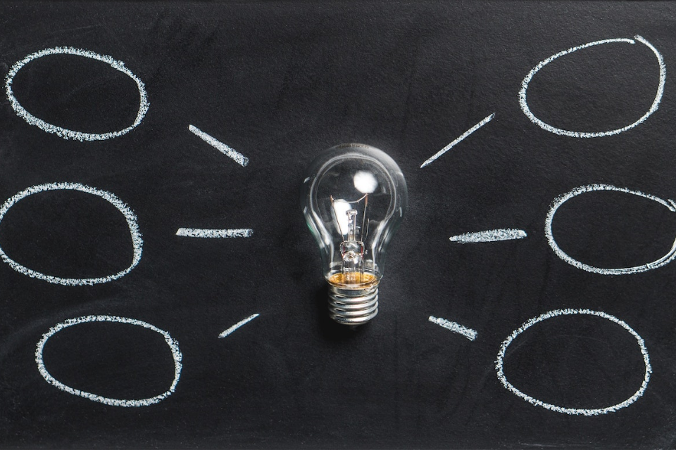Lightbulb laying on a black chalkboard with lines and bubbles around it