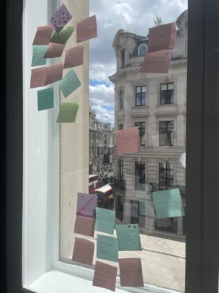 A picture of a window covered in different coloured sticky notes, there is the scene of a London street as you look through the window with clouds in the sky. This was a post-it exercise ran by Abby Wade (GCS Applied Innovation Manager) during a cross-department hackathon day, to gain diverse thoughts and perspectives on the future of digital capability in the organisation.