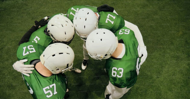 a group of American football players in green and white jerseys, all huddled together wearing white helmets
