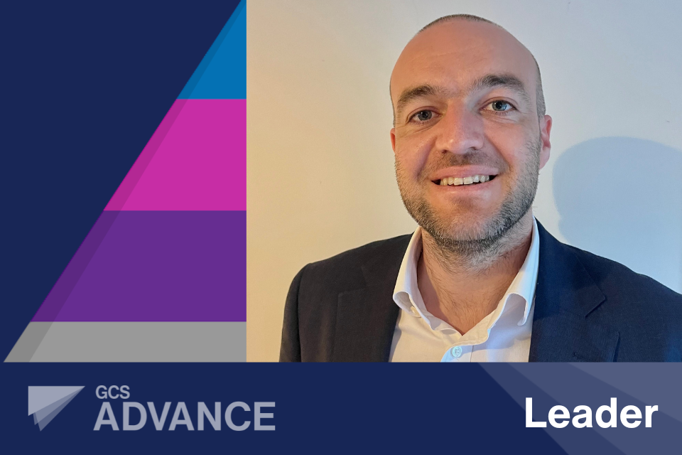 Selfie-style picture of Oliver Finlay-Smith, from Food Standards Agency learner on Advance Leader, with the 'Advance' logo and the word 'Expert' on a blue coloured banner layered over the top and the 'Advance' five tiered coloured pyramid behind on a dark navy background
