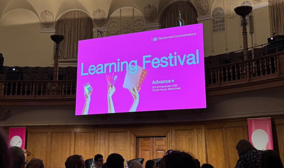 A stage and with a large screen on the wall displaying a pink slide and the words Learning Festival on it.