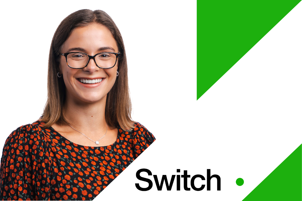 Ruby standing smiling to the camera. The background is a bright green and to the right is a white tilted rectangle with the 'Switch' logo.