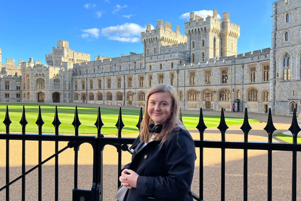 Abby Wade, Applied Innovation Manager, poses in front of a castle. She is holding a bag and smiling.