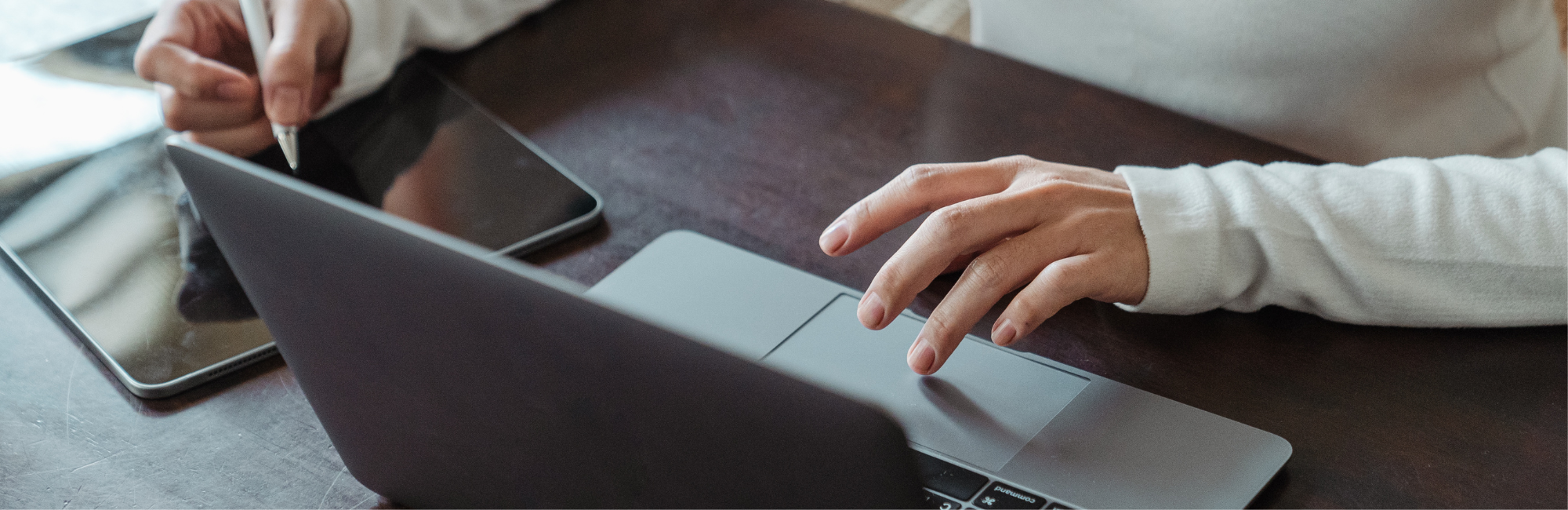 An individual seated at a desk utilizing a laptop and a tablet.