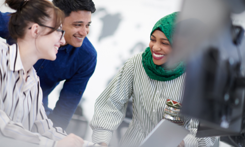 Three people are smiling at each other whilst working on a laptop.