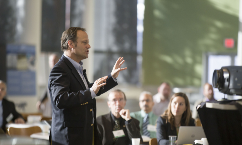 A person is standing and addressing a crowd of people that are sitting down.
