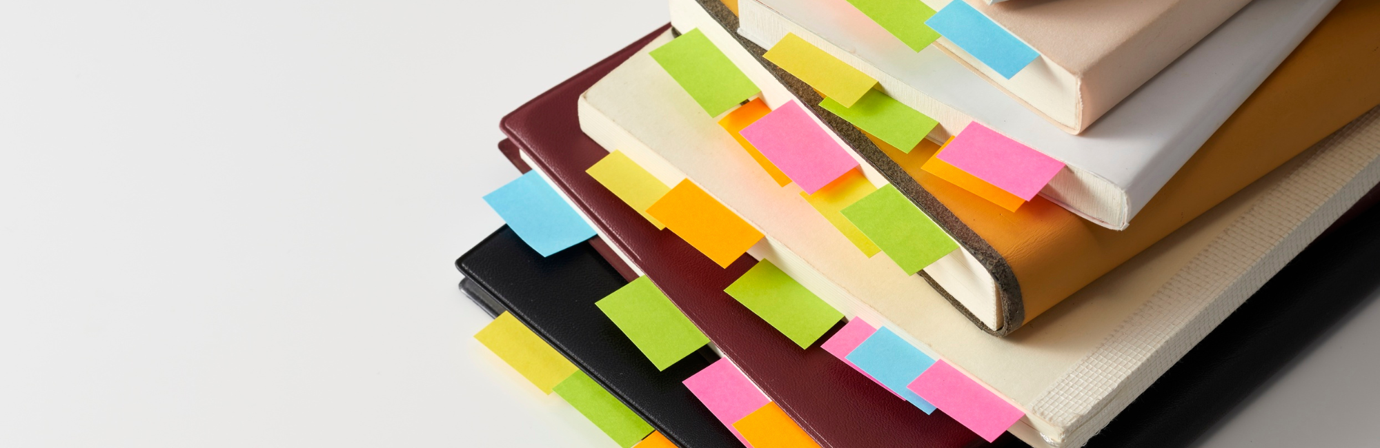 A stack of notebooks with sticky notes protruding from the pages.