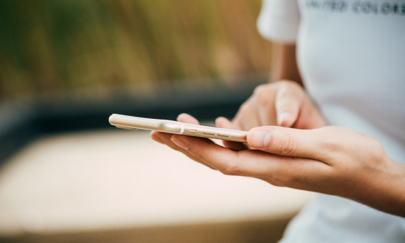 Close-up view of a person holding a smartphone horizontally with both hands and tapping the screen.